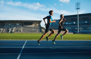 Two young men running on race track. Male professional athletes running on athletics race track.